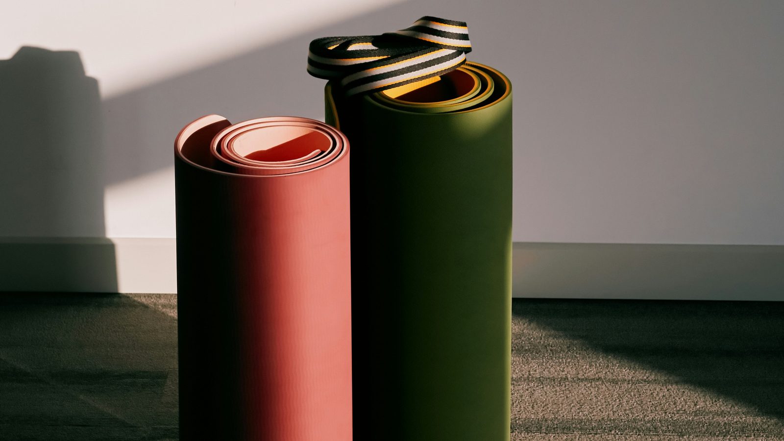 Two rolled exercise mats standing on a carpet in a patch of window light